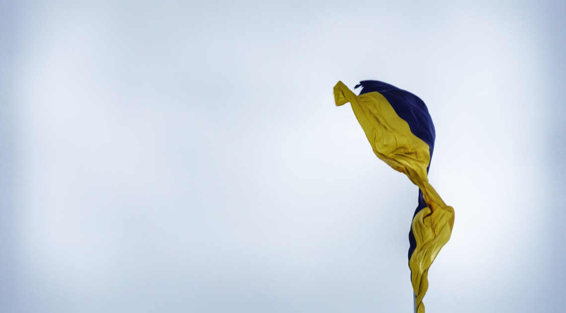 Eine ukrainische Flagge vor hellem Himmel (Foto: Vika Strawberrika/Unsplash)